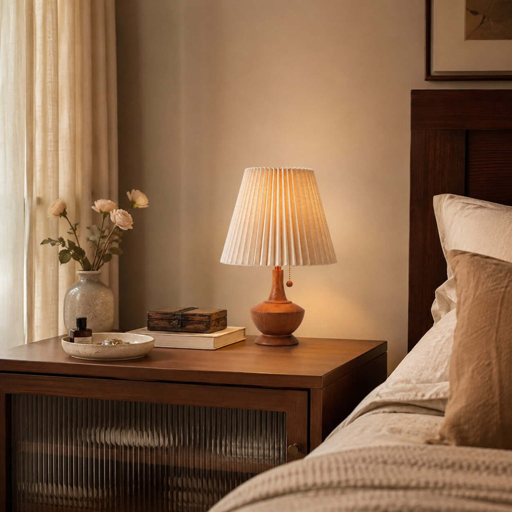 Clérachic lamp on a bedside cabinet with a ribbed glass door, next to a bed with linen bedding and a vase of pale roses.