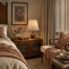 Clérachic lamp on a bedside cabinet with ribbed glass doors, in a bedroom with a pink throw and a framed botanical print.