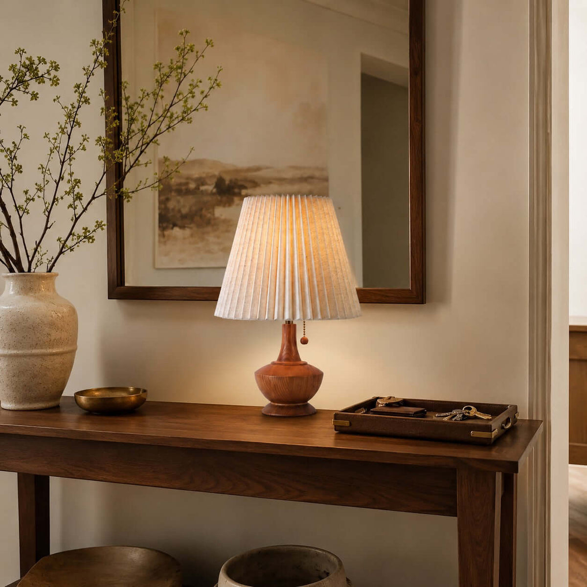 Close view of the Clérachic lamp on a wooden console under a framed mirror, with a vase of blossom and a tray of keys.