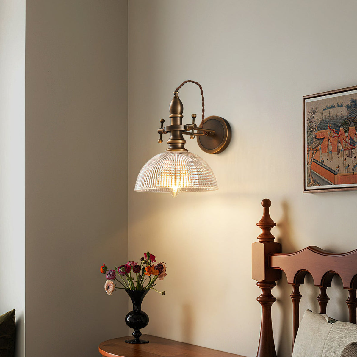Clear ribbed-glass dome shade lit on a Clérachic brass wall light above a bedside table with a vase of flowers.