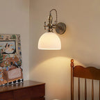 This Clérachic wall light with a ribbed white dome shade hangs beside a framed illustration and a wooden chair back.