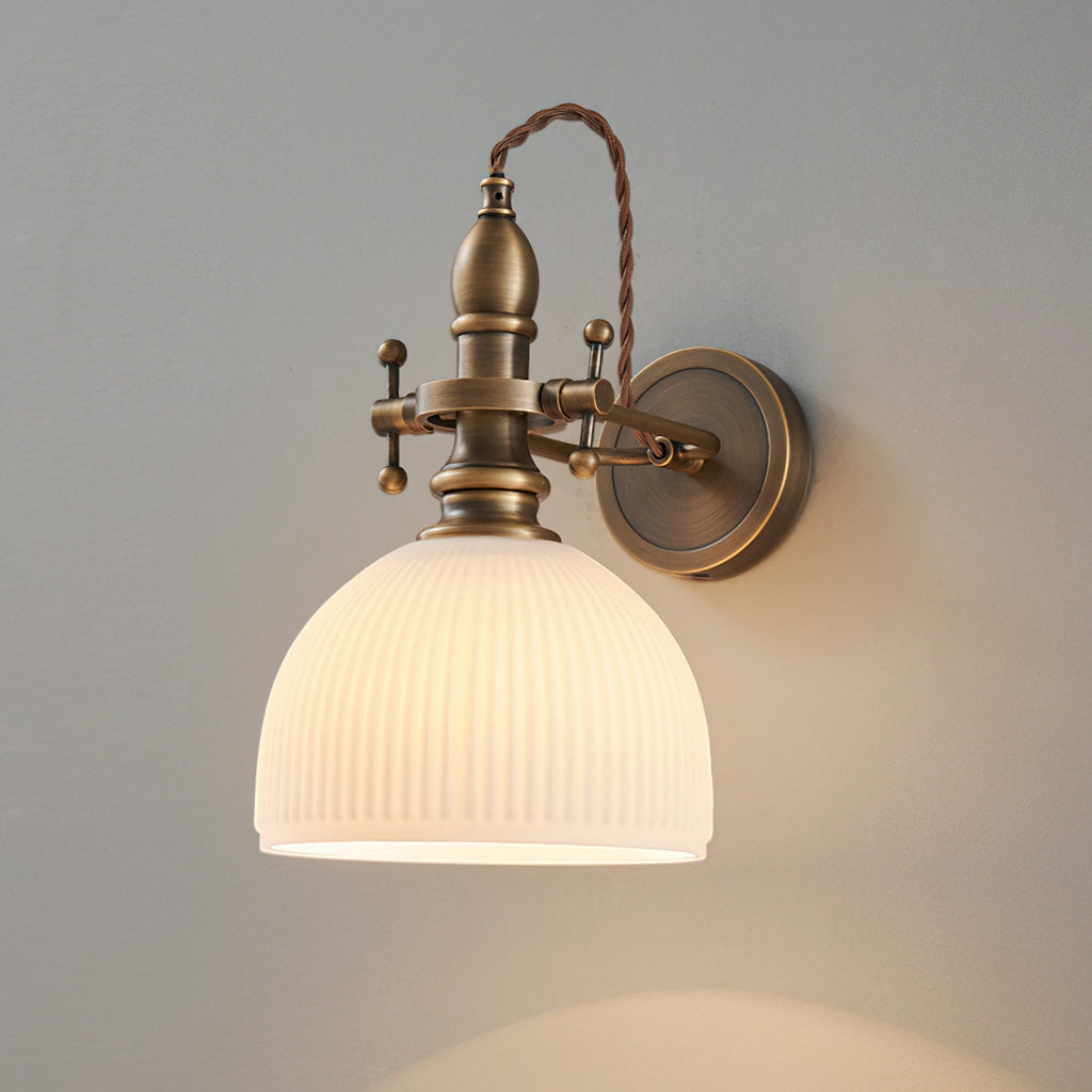 Ribbed white dome shade lit from within on a Clérachic wall light, its twisted brown cord arching over the brass stem.