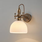 Ribbed white dome shade lit from within on a Clérachic wall light, its twisted brown cord arching over the brass stem.