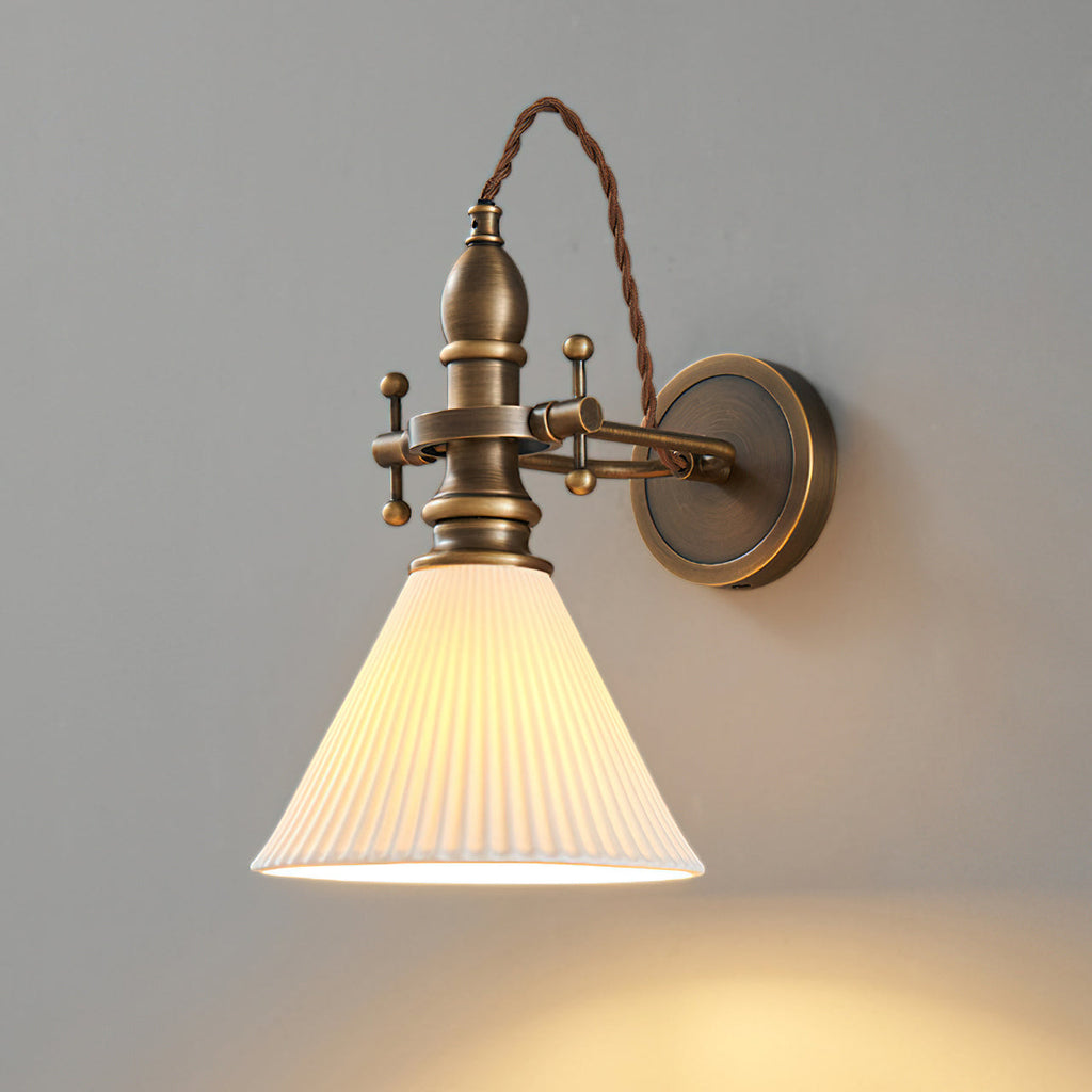 Pleated white cone shade casting a warm pool of light below this Clérachic wall light on a grey wall.