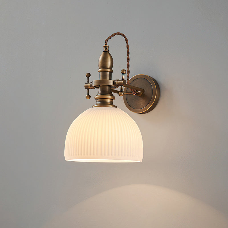 White ribbed dome shade on a Clérachic wall light, lit, with a soft arc of light below it on a grey wall.