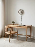 A taupe Clérachic ceramic wall light, unlit, hangs above a light oak desk and a woven-seat chair, next to sheer curtains.