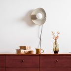 A taupe Clérachic ceramic wall light and white globe, switched off, above a wooden chest with stacked books and a glass vase.