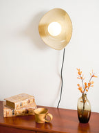 Lit close up, a Clérachic ceramic wall light glows buttery gold over a polished wooden chest holding old books and a mug.