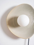 Close view of the crackled taupe glaze and thin gold rim on this Clérachic ceramic wall light, with the white globe at its centre.