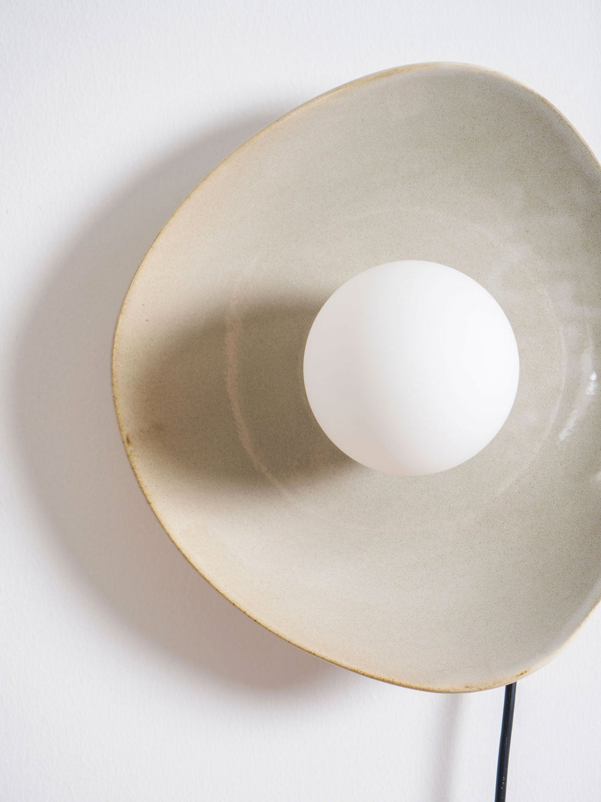 Close view of the crackled taupe glaze and thin gold rim on this Clérachic ceramic wall light, with the white globe at its centre.