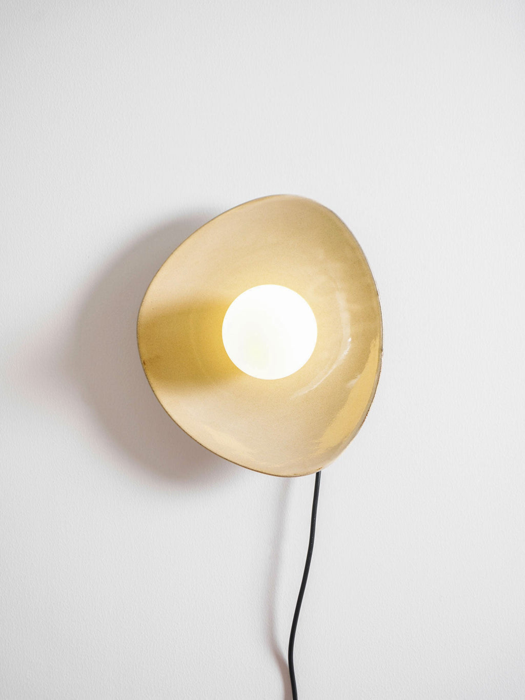 Lit, this Clérachic ceramic wall light shows a warm golden glow inside its disc and a soft shadow on the white wall.