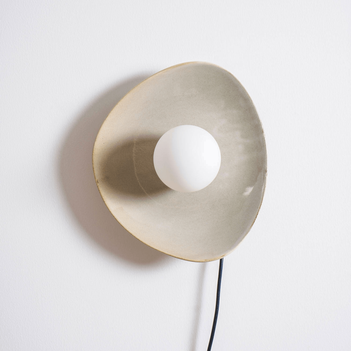 Large front view of the taupe glazed disc and white globe on this Clérachic ceramic wall light, with its cord dropping out of frame.