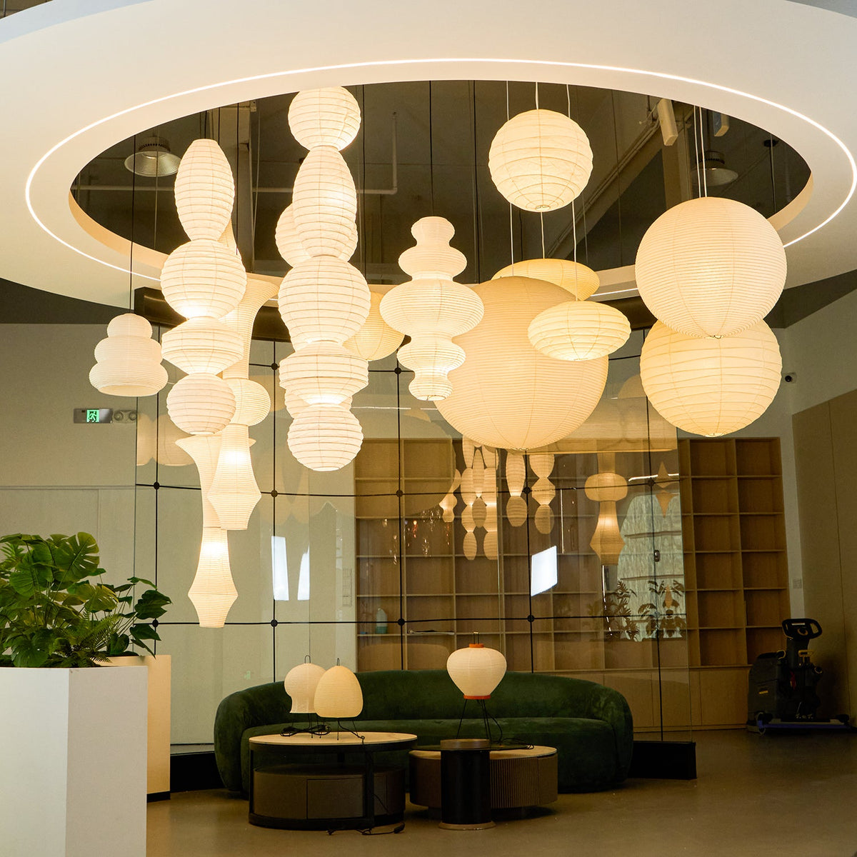 Clérachic paper lantern installation in the lobby, an illuminated exit sign and the seating below giving the scale of the hang.