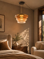 Amber glass tiers on this Clérachic pendant glow warmly beside a bed with velvet cushions.