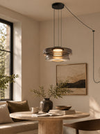 Smoke-grey glass tiers on this Clérachic pendant hang above a curved bench in a dining nook.