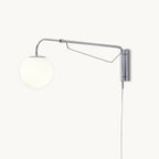 Front view of this Clérachic plug-in wall light on a white backdrop, with a chrome swing arm, a white globe and a slim cord hanging down.
