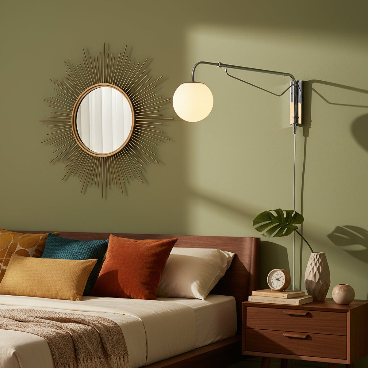 Chrome Clérachic swing-arm wall light with a white globe on a sage-green wall above a walnut bed, bedside drawers and a sunburst mirror.
