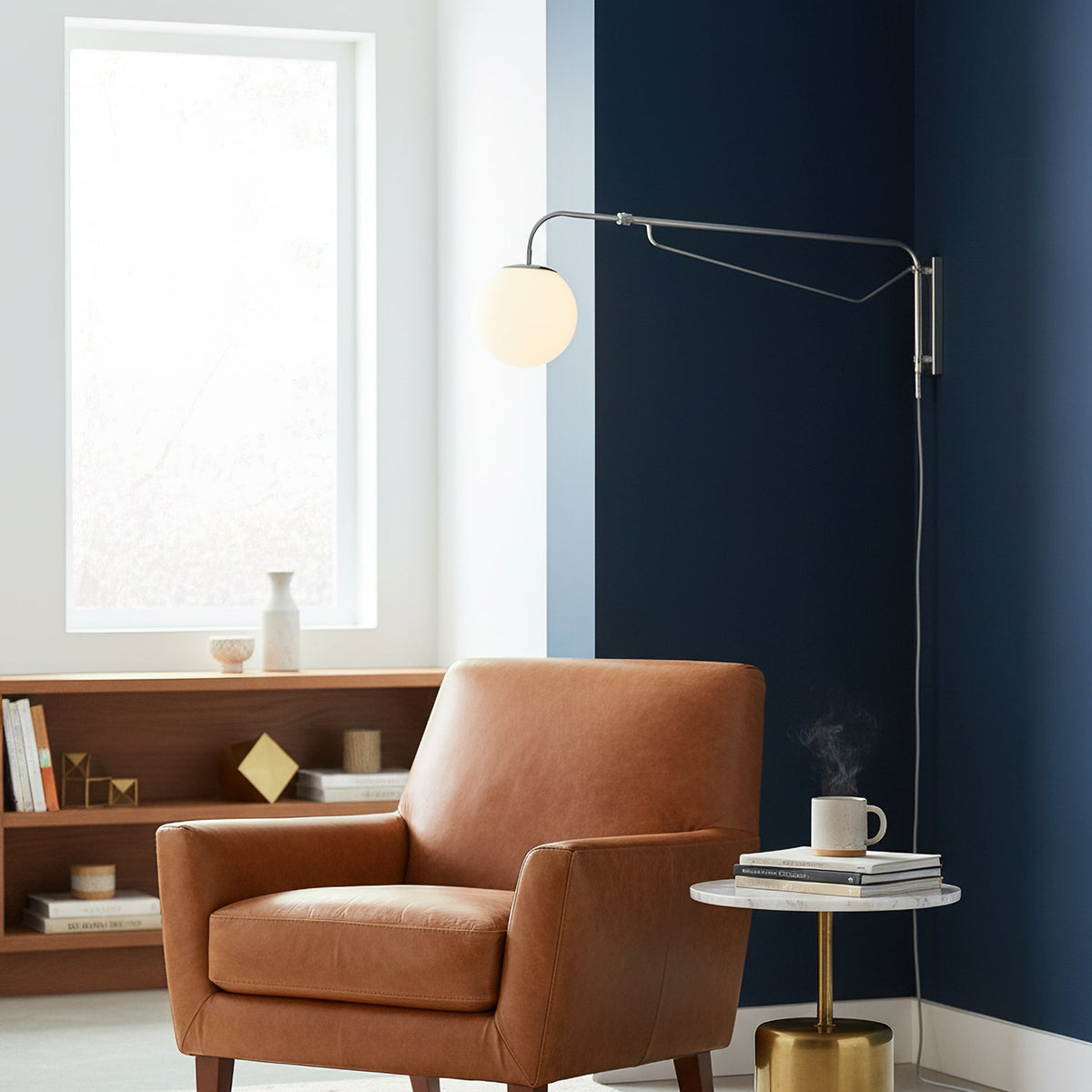 Chrome Clérachic wall light with a white globe where a navy wall meets a white one, above a tan leather armchair and a brass side table.