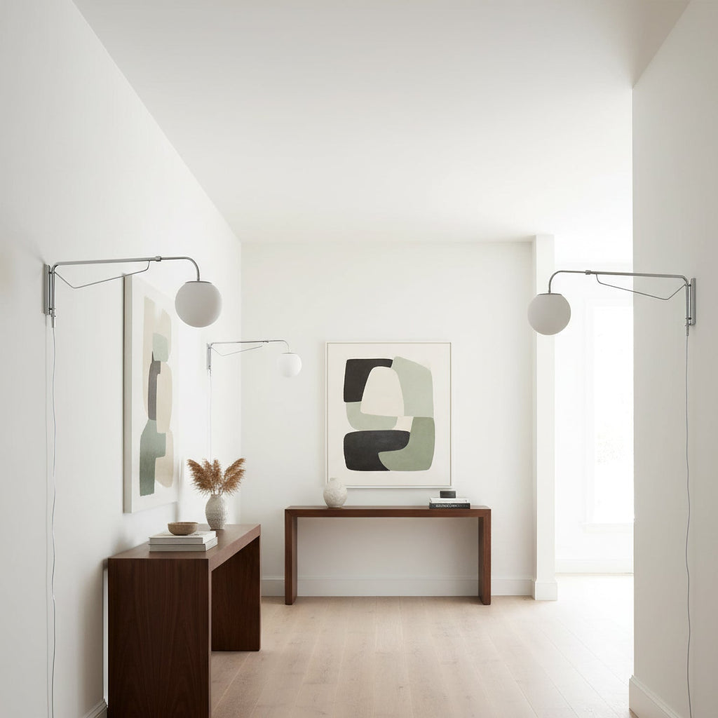 Two chrome Clérachic wall lights with white globes in a bright white room, over walnut consoles and a framed abstract print.