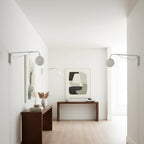 Two chrome Clérachic wall lights with white globes in a bright white room, over walnut consoles and a framed abstract print.