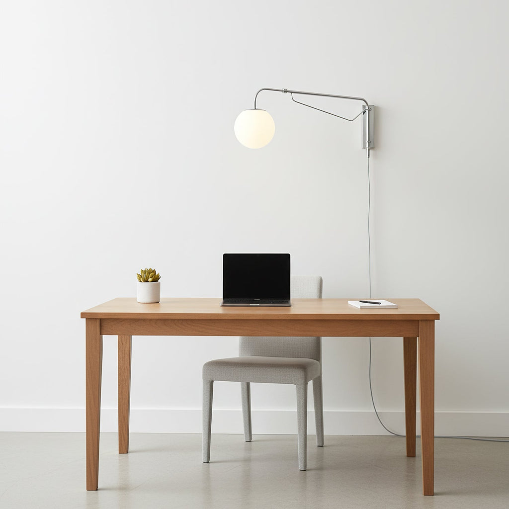 Clérachic wall light with a chrome arm and white globe above a plain wooden desk with a laptop and a small plant.