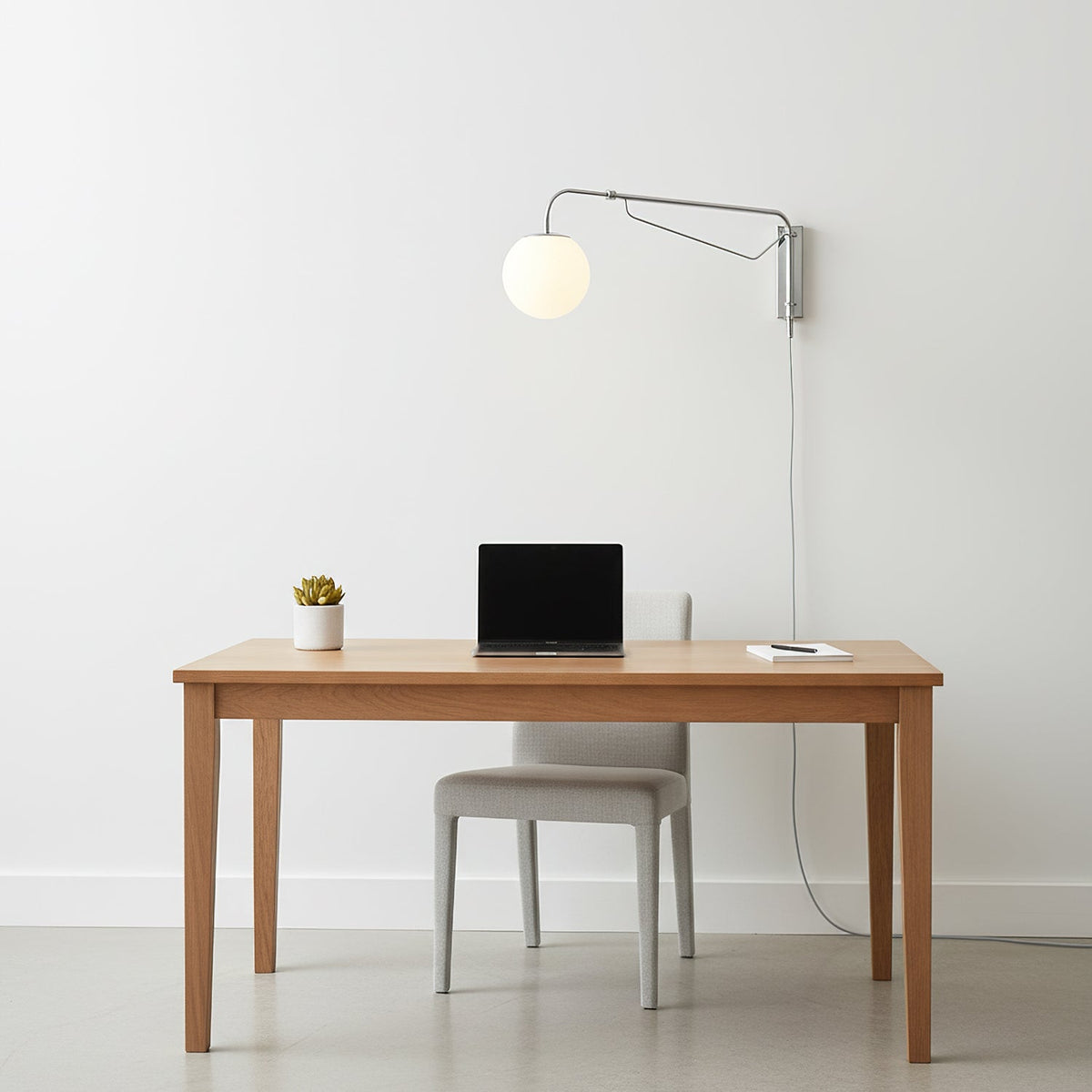 Clérachic wall light with a chrome arm and white globe above a plain wooden desk with a laptop and a small plant.