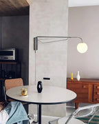 A chrome Clérachic wall light with a white globe on a pale concrete-look wall, above a round white table and a walnut sideboard.