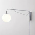 Close view of this chrome Clérachic wall light on a white wall, showing its long arm, diagonal brace and white globe.