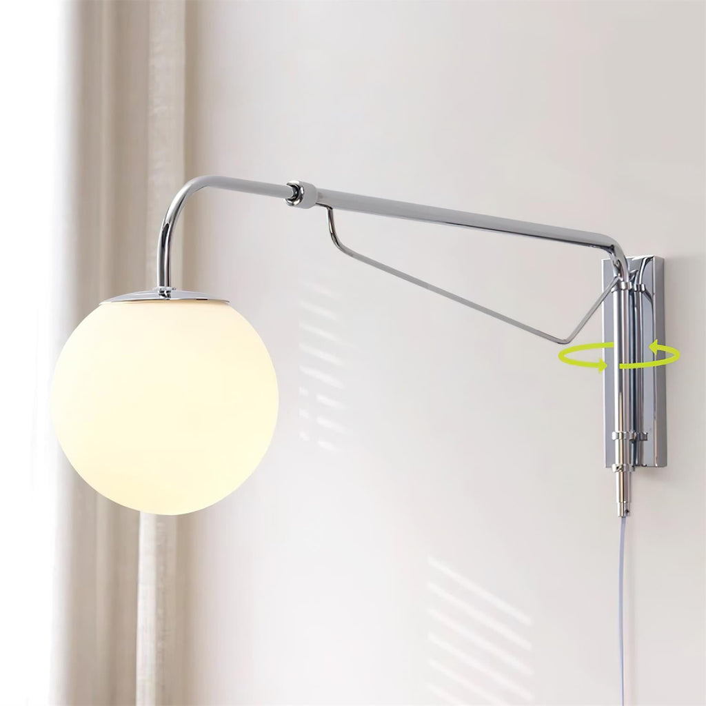 Chrome Clérachic wall light with a lit white globe by a beige curtain, shown with a green arrow marking its swivel at the wall plate.