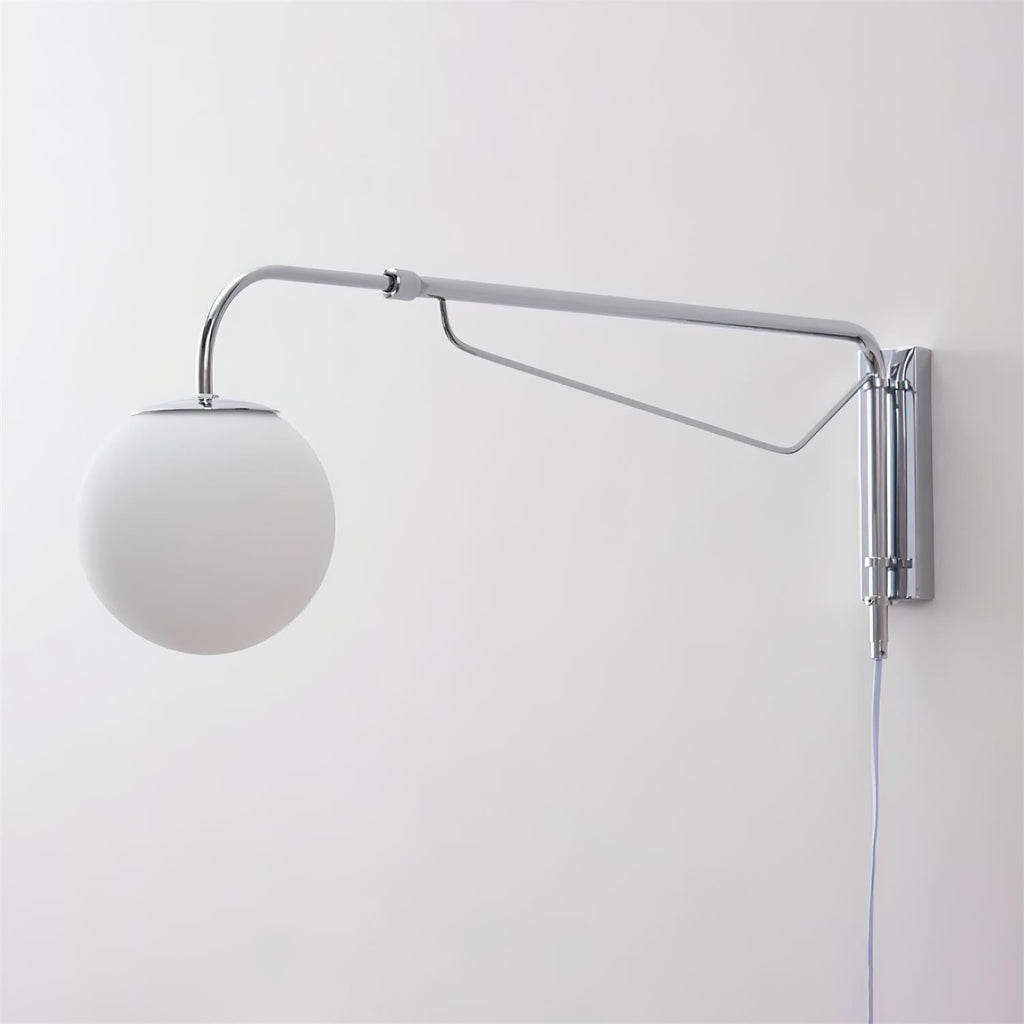 Unlit chrome Clérachic wall light with a matt white globe on a pale wall, with its cord hanging below the mounting plate.