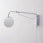 Unlit chrome Clérachic wall light with a matt white globe on a pale wall, with its cord hanging below the mounting plate.
