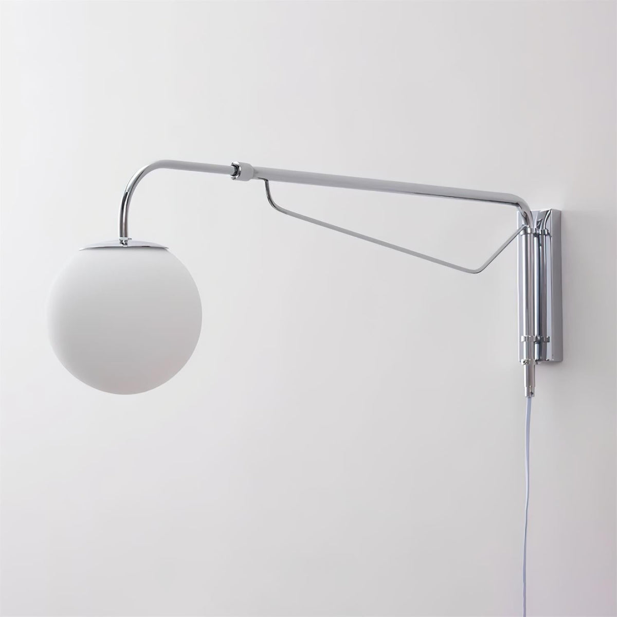 Unlit chrome Clérachic wall light with a matt white globe on a pale wall, with its cord hanging below the mounting plate.