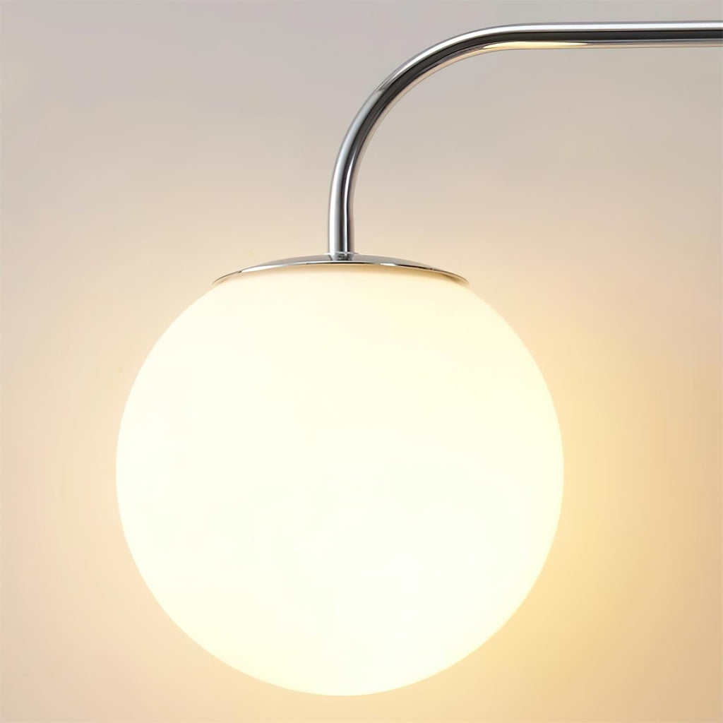 Close view of a lit white globe with a chrome fitting and a curved chrome arm on this Clérachic wall light, in warm light.