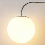 Close view of a lit white globe with a chrome fitting and a curved chrome arm on this Clérachic wall light, in warm light.