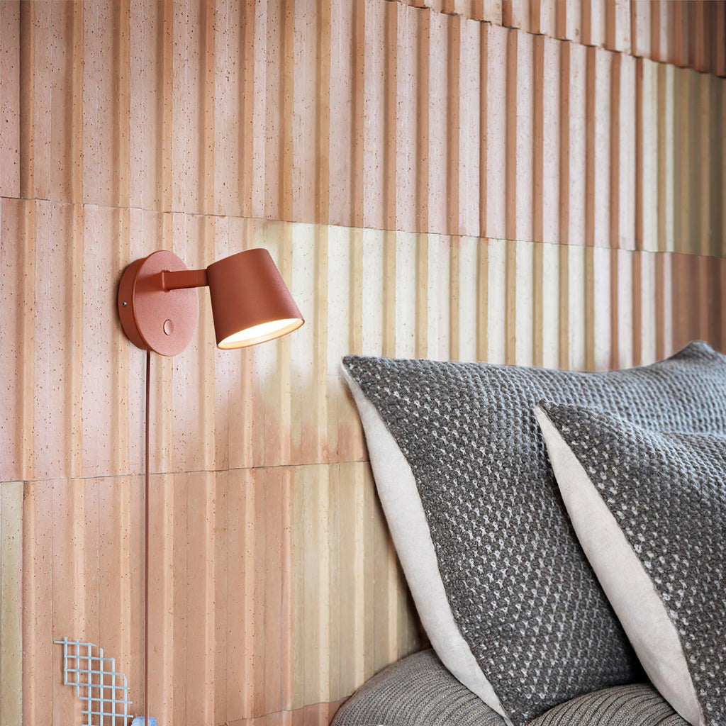 Red Clérachic wall light shining on a ribbed blush-pink wall above grey knitted cushions.
