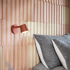 Red Clérachic wall light shining on a ribbed blush-pink wall above grey knitted cushions.
