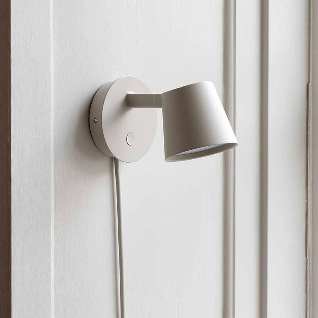 Close view of the matte white round backplate, arm and tilted cone shade on this Clérachic wall light.