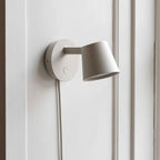Close view of the matte white round backplate, arm and tilted cone shade on this Clérachic wall light.