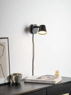 Black Clérachic wall light on a white wall above a dark chest of drawers, with a book, a mug and a ribbed candle.