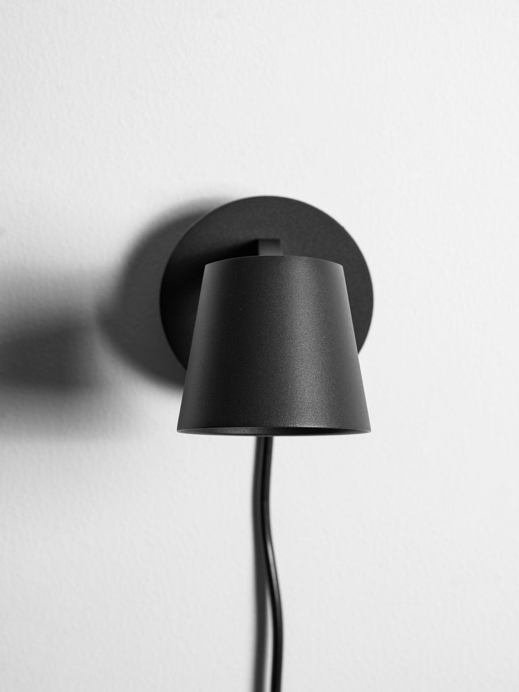 Rear of the cone shade on this black Clérachic wall light, seen close up against its round backplate on a white wall.
