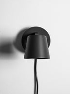Rear of the cone shade on this black Clérachic wall light, seen close up against its round backplate on a white wall.