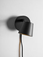 Black Clérachic wall light with the shade swung low in front of the backplate, close up on a white wall.
