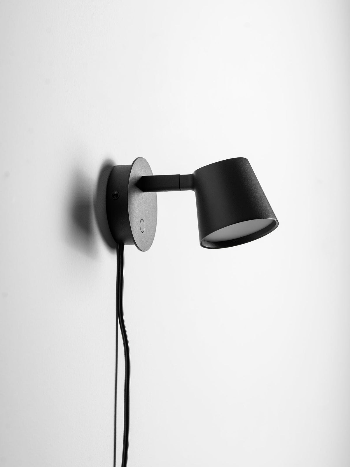 Side view of the black Clérachic wall light showing the slim arm joining the round backplate to the shade, with the cord below.