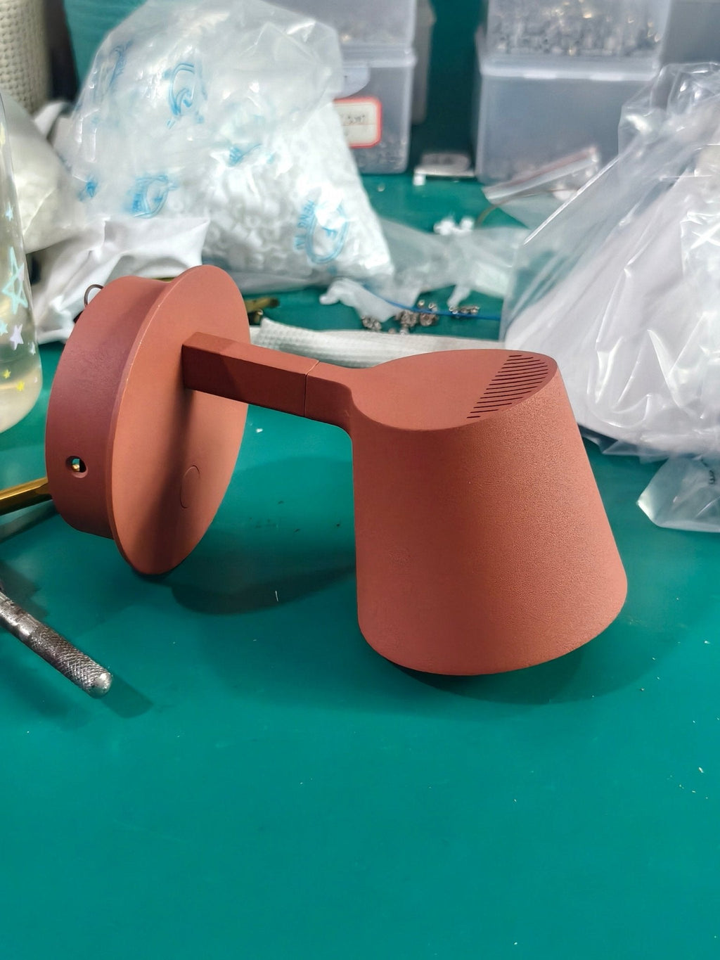 Red Clérachic wall light on a workbench, shown side-on with a round backplate, a short arm and a vented shade.