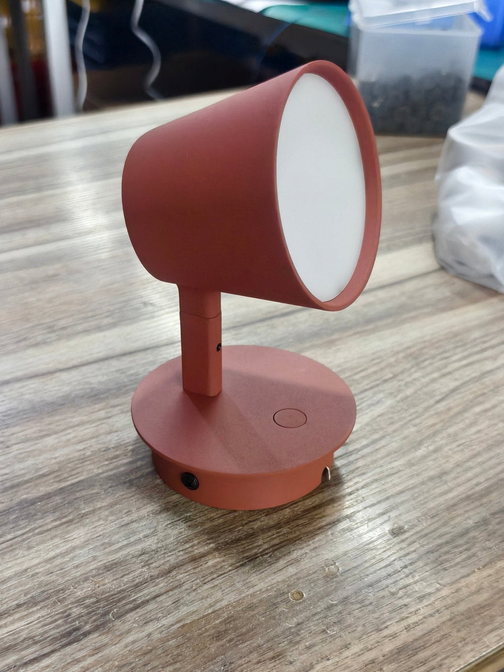 Red Clérachic wall light on a wooden table, its frosted white diffuser facing forward and the shade tilted up.