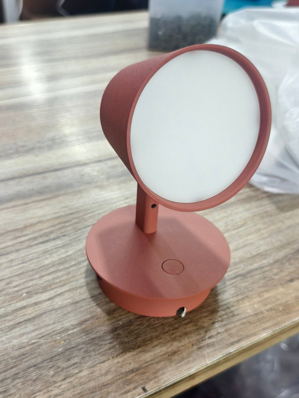 Red Clérachic wall light on a wooden table, showing the round white diffuser inside the cone shade.