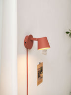 Red Clérachic wall light angled over the wall, a red cord running down beside a pinned postcard and a warm glow below the shade.
