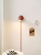 Lit red Clérachic wall light on a cream wall, a red cord below it and a checkered mug on the side table.