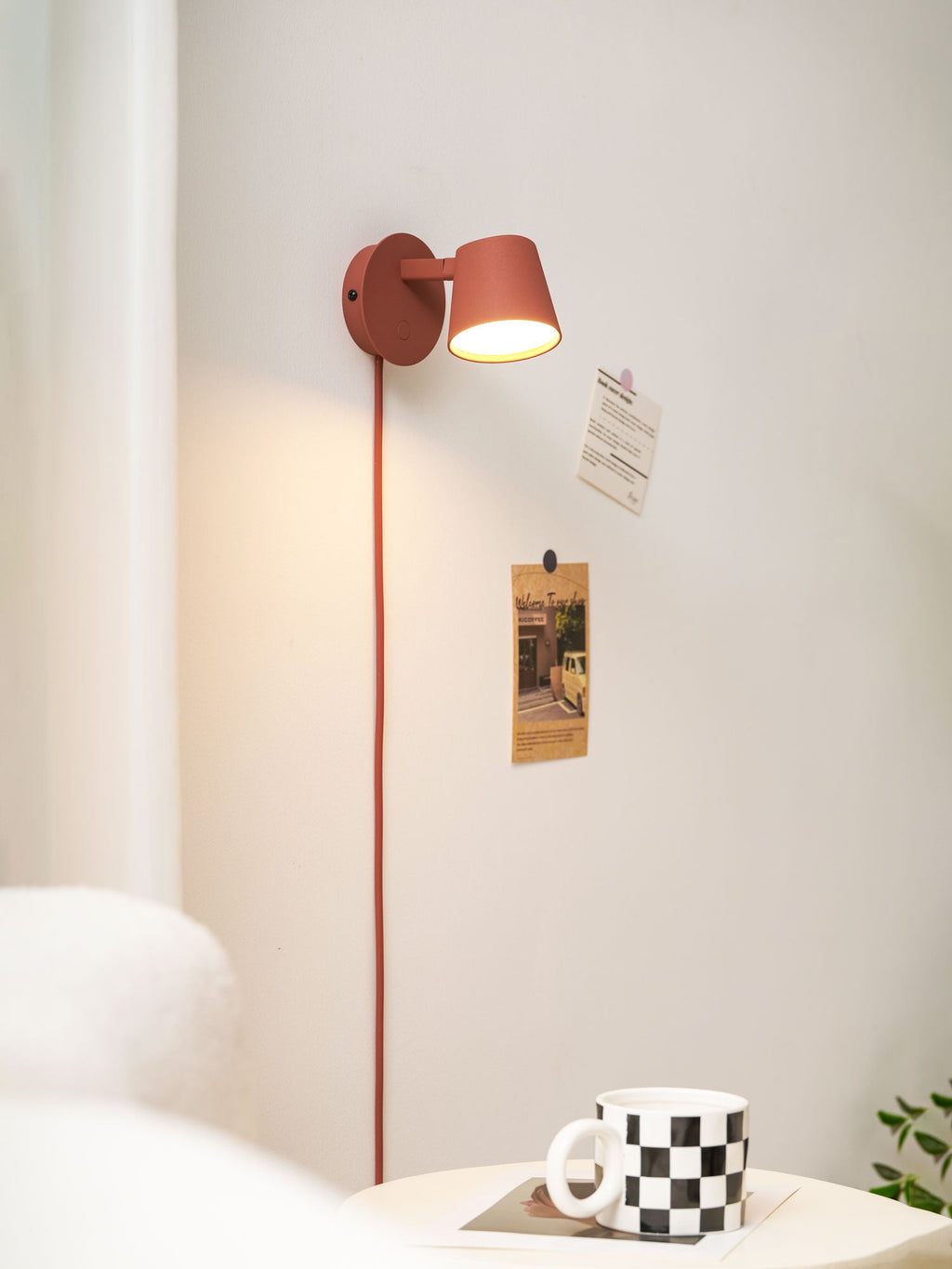 Red Clérachic wall light with its shade turned to the side, a warm glow and two postcards pinned to the wall.