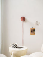 Small red Clérachic wall light with its cord running straight down a white wall to a ribbed side table and a checkered mug.